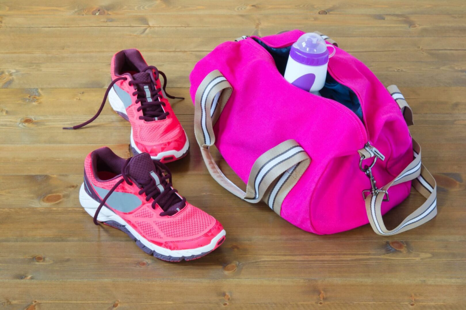 Pink gym bag and running shoes on floor.